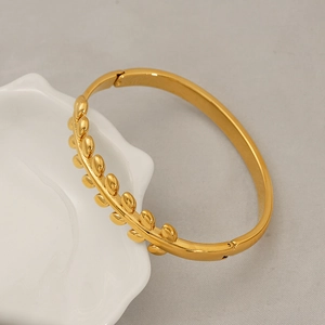 Detailed close-up of a gold leaf cuff bracelet displayed on a white ceramic petal dish