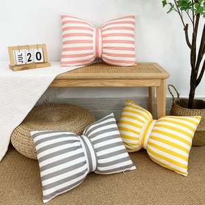 Three bow-shaped velvet cushions in pink, gray, and yellow stripes on a cozy bench