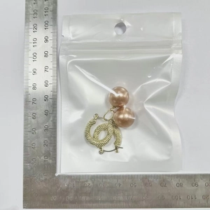 Detail view of champagne pearl earrings with gold twisted C-shape on measuring scale