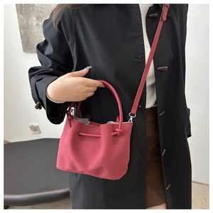Red suede bucket bag styled with a black coat to show the carry size and visual contrast