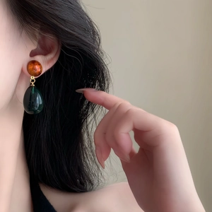 Close-up of asymmetrical orange and dark green resin waterdrop earrings on a model