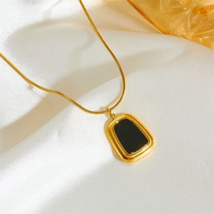 Détail d'un collier doré avec pendentif rectangulaire noir sur un tissu en soie blanche