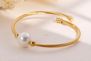 Détail du bracelet torsadé doré avec une grande perle blanche et des billes polies