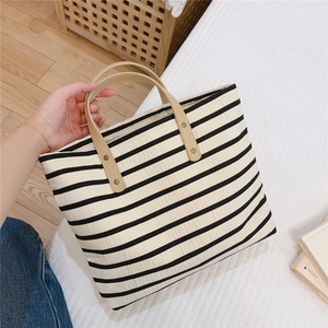 Detail of striped canvas tote bag featuring brown leather handles and metal rivet fasteners