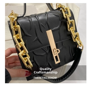 Detail of black textured leather bag with gold metal clasp and large chain handle