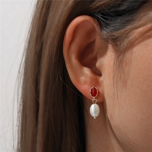 Macro detail of a vintage pearl earring with red marquise gemstone on a silver hook