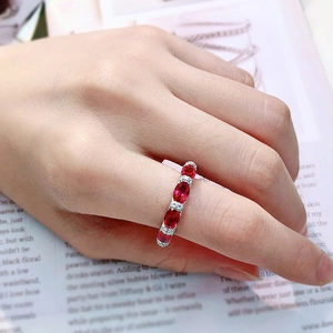 Close-up of a silver ring with oval red gemstones and diamonds on a model's hand