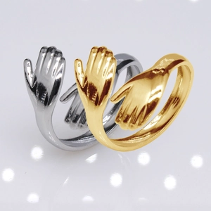 Detail of interlocking gold and silver hugging hands rings on a gray reflective surface