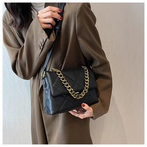Detail van zwarte gewatteerde crossbodytas met gouden ketting gedragen door model