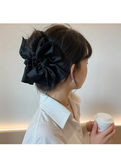 Macro view of a large black satin bow hair claw clip worn on a low bun hair style
