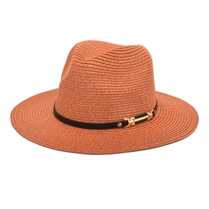 Macro shot of burnt orange woven straw fedora with brown leather band and gold buckle