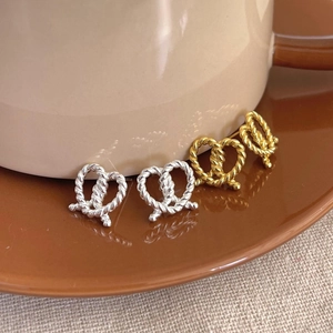 Close-up of twisted knot heart earrings in silver and gold on a coffee cup