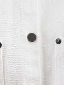 Close-up of white twill fabric and dark gray metal buttons on a denim vest