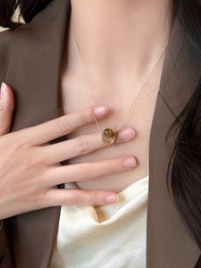 Close-up of a U-shaped gold necklace with a brown tiger eye bead on a model's neck