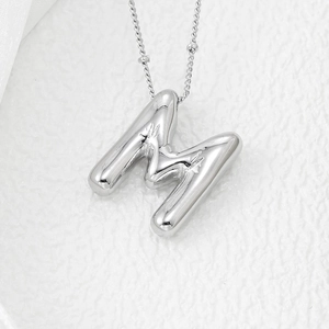 Macro shot of 3D balloon letter M pendant in polished silver on a textured stone surface