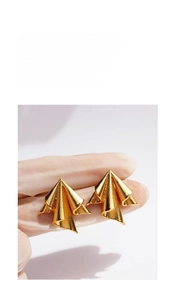 Detailed macro view of gold geometric earrings with folded metal texture held in hand