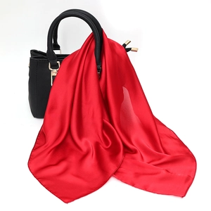 Detail of red satin scarf draped over a black leather handbag with a high-shine finish