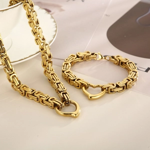 Golden Byzantine chain necklace and bracelet set with heart clasp on elegant beige surface