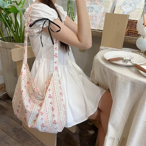 Detail view of large canvas floral crossbody bag worn over a white puff sleeve dress