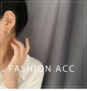 Close-up of golden geometric multi-hoop earrings worn against textured gray backdrop