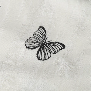 Distressed knit beanie with black butterfly embroidery on white textured fabric