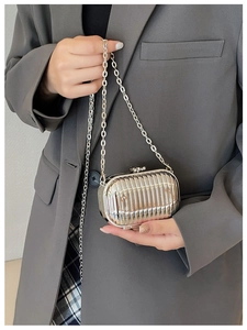 Silver mini suitcase chain bag with vertical stripes held by a model in a grey blazer