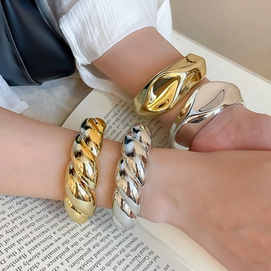 Close-up of golden and silver twisted acrylic cuff bracelets on a model's arm