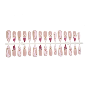Pink almond press-on nails set with 3D floral accents and gold beads on white stand