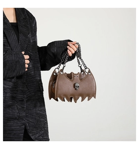 Detail of a brown bat-shaped gothic crossbody bag with skull charm and silver chain