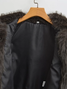 Detail view of dark grey faux fur vest with black silky lining and care label on wood hanger