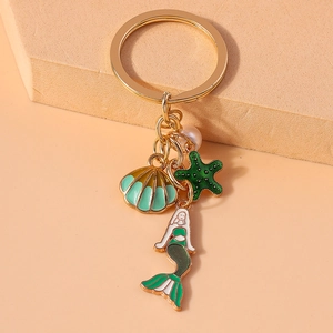 Detailed shot of mermaid, starfish, and shell enamel charms on a gold keychain with pearl