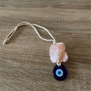 Detail of handmade woven necklace featuring pink crystal stone and blue evil eye charm