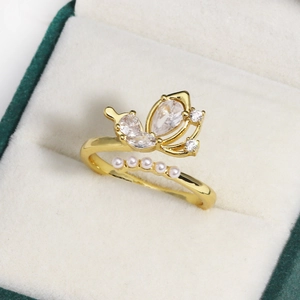 Close-up of golden butterfly ring featuring zircon stones and mini pearls on green velvet