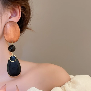 Detail of wooden oval stud and black teardrop drop earring worn by a model