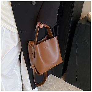 Detail of brown leather bucket bag held by hand with brand logo engraving at the bottom