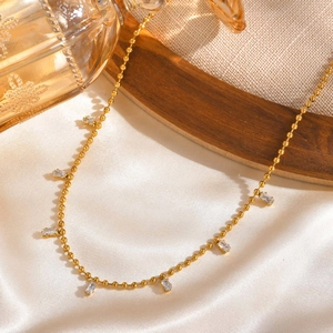 Gold stainless steel beaded chain necklace with seven square white zircons on silk background