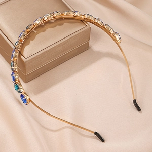 Detailed shot of golden headband with blue and green gems on a soft beige silk background