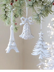 White flocked Christmas ornaments set hanging on pine branches with warm bokeh lights