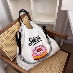 Detail shot of a white nylon tote bag with pink donut embroidery and braided strap