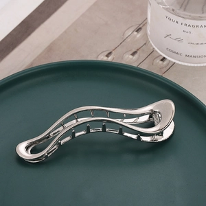 Silver wavy metal hair claw clip displayed on a luxury ceramic plate background