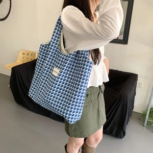 Close-up of blue and white checkered canvas tote bag with woven texture worn by model