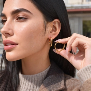 Close-up of model wearing large gold-plated stainless steel hoop earrings with polished finish