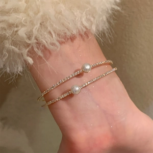 Close-up of double-layer golden cuff bracelets with sparkling zircons and white pearls