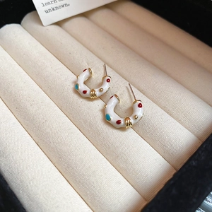 Close-up of C-shaped enamel earrings with red and blue dots in a velvet jewelry box