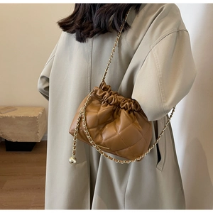 Close-up of brown quilted bucket bag with gold chain strap on a beige coat model