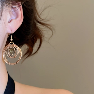 Detail of round tiger eye stone drop earring on model featuring layered golden rings