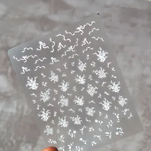 Adesivi per unghie in pizzo bianco con fiori sottili e fiocchi su sfondo grigio