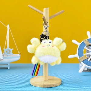 Cute yellow plush crab keychain with rainbow ribbon hanging on a mini wooden stand