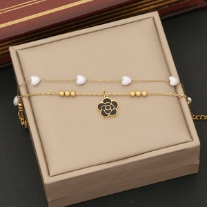 Détail d'un bracelet doré double couche avec perles de cœur blanches et pendentif fleur noire