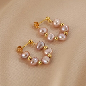 Macro detail of round earrings featuring pink baroque pearls and gold beads on fabric